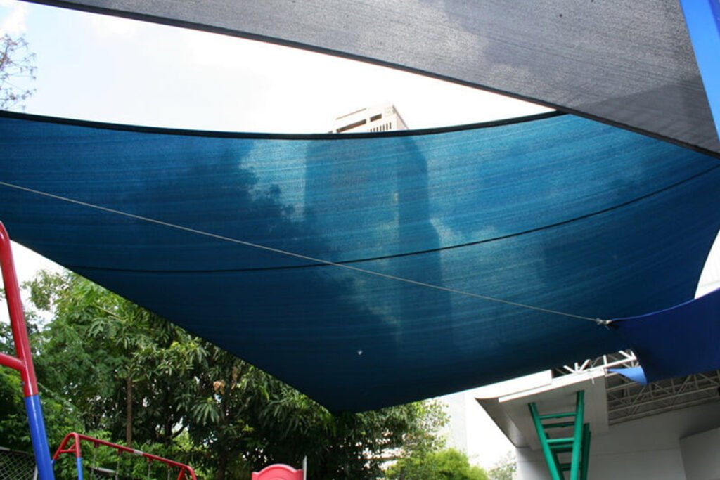 Mặt dưới cánh buồm vải xanh dệt thưa nhìn ngược lên, mây trời in qua lớp vải, mép cánh xám phía trên