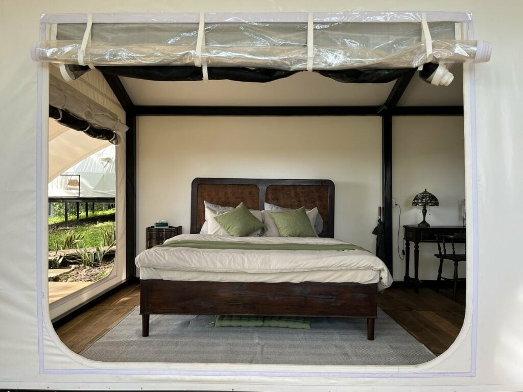 Giường gỗ đầu mây trong lều Garden View Tent, tấm bạt trong cuộn trên cửa, bàn đèn kính màu